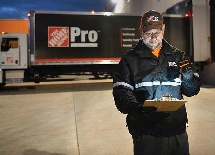 Home Depot driver reviewing his manifest on a clipboard in front of a Home Depot Pro truck