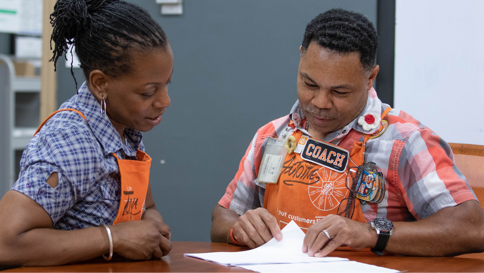 Two store associates look over paperwork on a table.