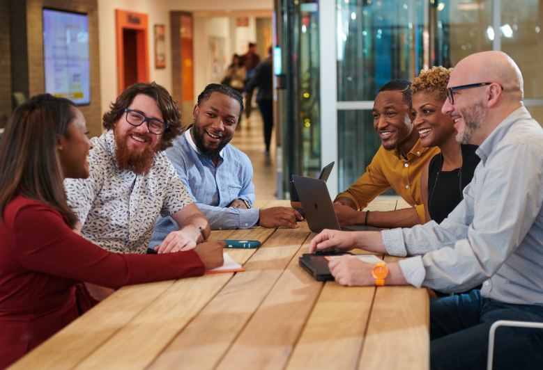 A group of corporate employees chat at a long table.