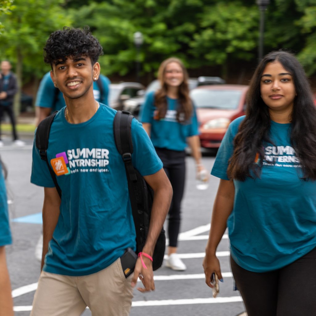 Male and female intern in teal shirts smiling while walking