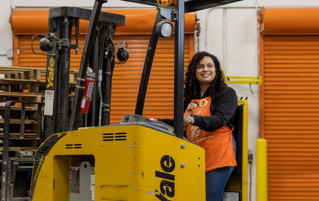 A young Latina women in an orange apron smiles while standing in a storage facility.