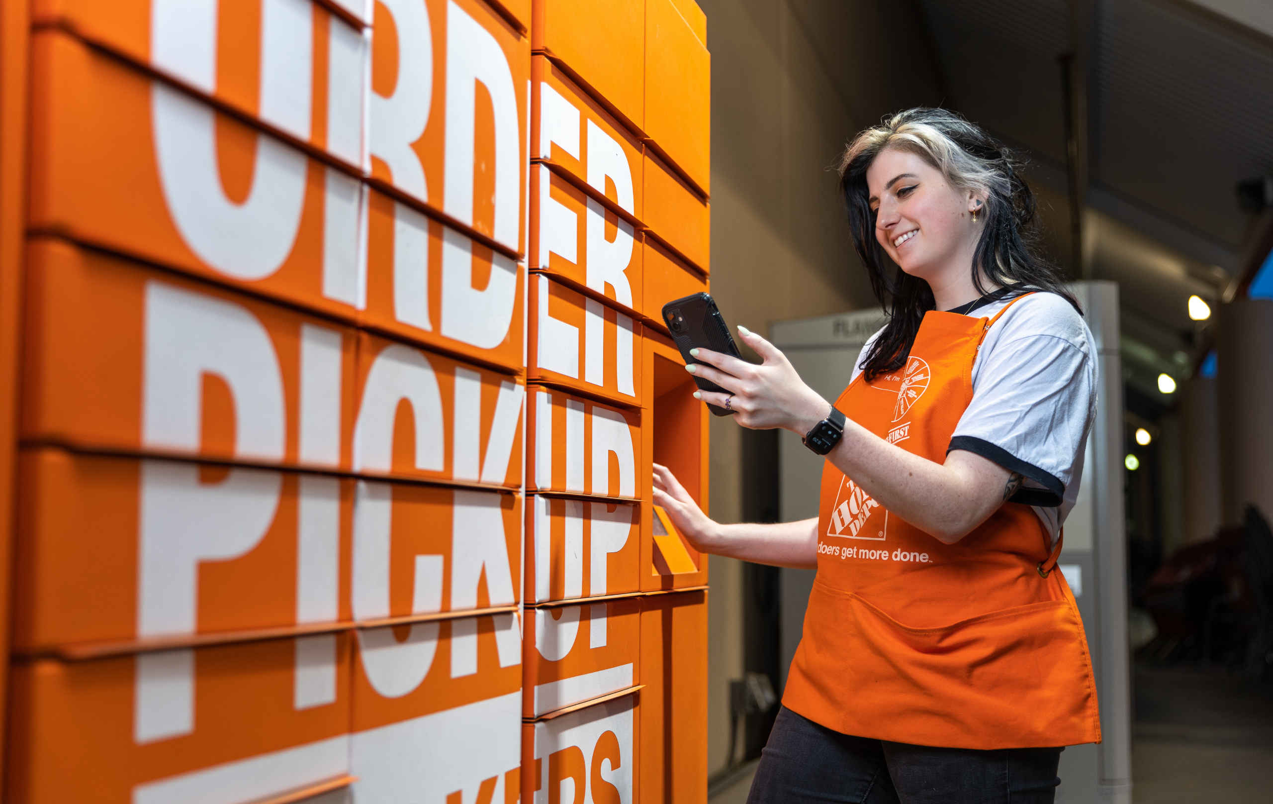 Man in Home Depot apron, smiling and moving a box down a conveyer in the warehouse